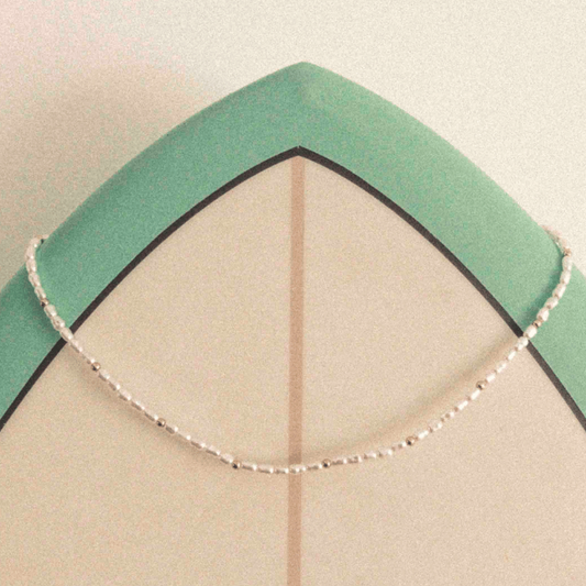 Perlenkette mit goldenen Details auf Surfbrett – Wild Tides Ocean Whisper
