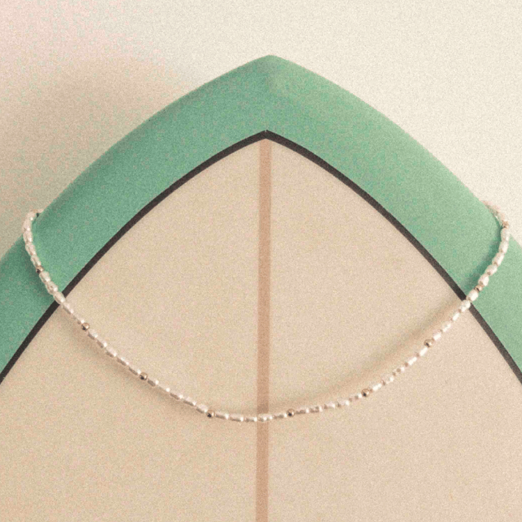 Perlenkette mit goldenen Details auf Surfbrett – Wild Tides Ocean Whisper